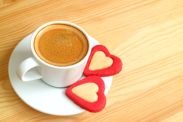 Cup of espresso coffee with a pair of heart shaped cookies served on wooden table