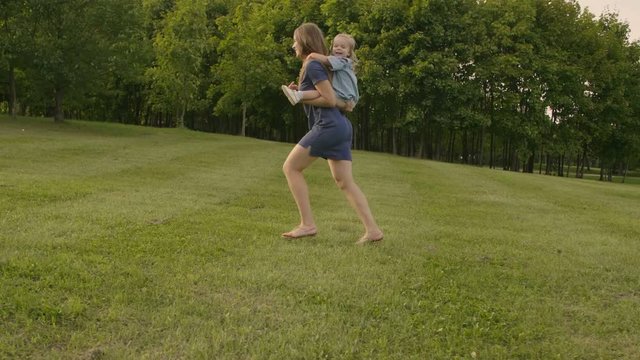 Daughter riding on mother in a city park at sunset. Slow motion