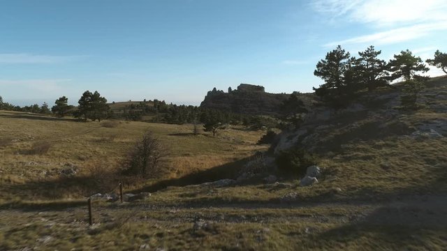 Path to rocky hills across forest and green valley. Shot. Coniferous trees under blue sky.