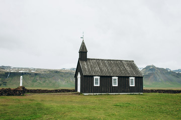 Black wooden church in Iceland against the background of the mountains. Budir Church.