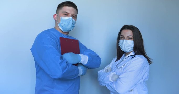 In the hospital (clinic) Two young doctors in lab coats a nurse and a doctor with a folder in their hands, scratching the synchron hands. Concept of: Medical mask, Medical gloves, Man, Woman.