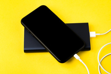 Smartphone charging with power Bank via USB cable on yellow background top view.