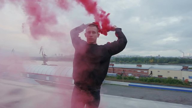 Millennial extraordinary man keep smoke torches in his hand and practice vogue dance choreography on the rooftop. A lot of colorful purple smoke. Concept of creative imagination and freedom mind
