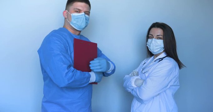 In the hospital (clinic) Two young doctors in lab coats a nurse and a doctor with a folder in their hands, scratching the synchron hands. Concept of: Medical mask, Medical gloves, Man, Woman.
