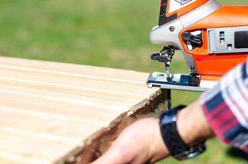 Carpenter using electric jigsaw outdoors, closeup.