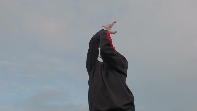 Millenial high-minded man practice original street dance outdoor on the sky background. He makes special unusual moves with his hand and neck by the music rythm.