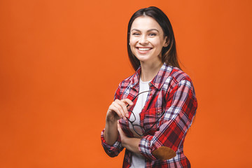 Smiling brunette woman in eyeglasses and casual posing with crossed arms and looking at the camera over orange background.