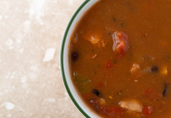 Top close view of a bowl of chicken tortilla soup on a marble table.