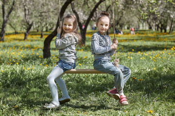 Two cute sisters on a swing together in a beautiful summer garden