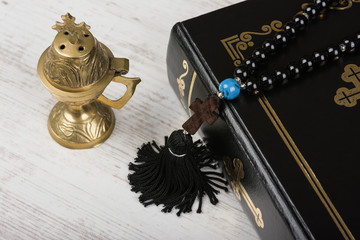 Closeup of Holy Bible, rosary beads with cross and incense burner on white wooden background. Religion concept and faith