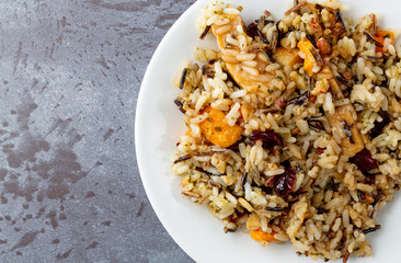 Top close view of chicken with pecans and wild rice on a plate atop a gray background