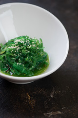 Chuka salad topped with sesame seeds and served in a white bowl, closeup on a dark brown stone background