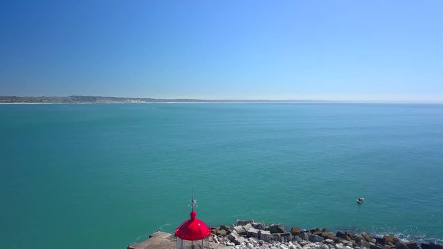 Aerial, reverse, drone shot, of Bugio lighthouse, on a rocky island, at the atlantic ocean, on a sunny day, near the Oeiras coast and Tejo river, in Lisbon, Portugal