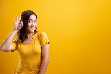 Happy woman showing OK gesture isolated on yellow background