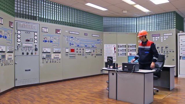 engineer gets up and approaches main control panel of gas compressor station, wide angle