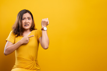 Shocked woman holding hand with wrist watch isolated on a yellow background