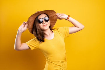 Portrait woman wearing sunglasses and hat isolated over yellow background