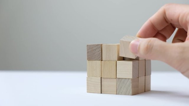 Hand to complete last piece wood cube for a bigger block