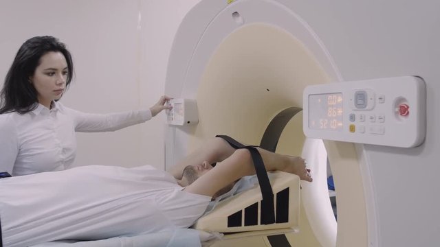 Beautiful nurse switch on ct-scan for diagnostics scanning procedure. Working medicine equipment, researcher technology, computer tomography in clinic. Tomograph moving with young male patient