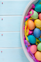 Dyed Easter eggs in a dish with colorful paper ribbons and sugar sprinkle confectionery dots on wooden blue surface.