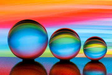 A row of three crystal balls with multicolored light painting behind them