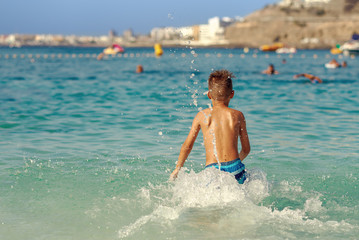 Cute European boy is jumping in to the sea, making numerour splashes around him. He is on his summer vacations.