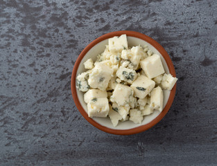 Portion of crumbled blue cheese on a in a small bowl atop a gray background