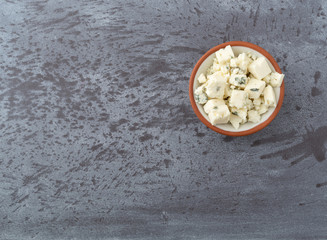 Portion of crumbled blue cheese on a in a small bowl offset on a gray background