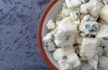 Portion of crumbled blue cheese on a in a small bowl atop a gray background top close view