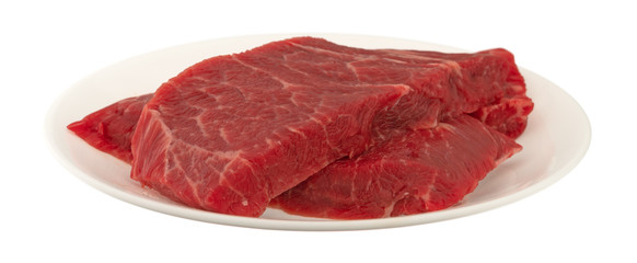 Slices of beef chuck boneless short rib steak on a plate atop white background side view
