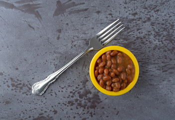Bowl of baked beans with bacon in a tomato sauce on a gray background with a fork to the side