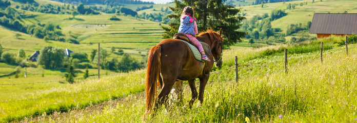 Lovely equestrian - little girl is riding a horse, mountain in the background