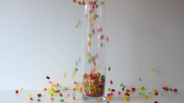 Colorful abstract video with sweets and candies. Empty clear jar which is being filled with thousands of colorful jelly beans poured into it from above in slow motion