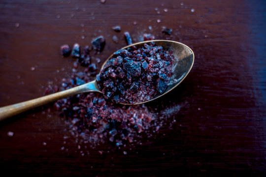 Raw organic rock salt or sendha namak or kala namak in a golden spoon on wooden surface.