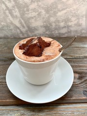 Coffee with foam and chocolate marshmallows.  White Cup with saucer and spoon, on wooden background.