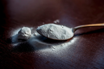 Raw baking soda or baking powder in a golden colored spoon on wooden surface.