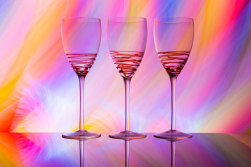 Three empty wine glasses in a row with colorful light painting behind