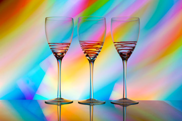 Three empty wine glasses in a row with colorful light painting behind