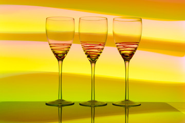 Three empty wine glasses in a row with colorful light painting behind