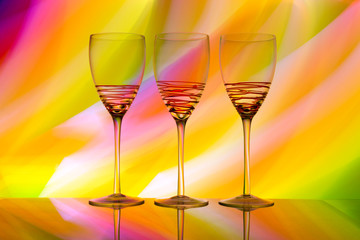 Three empty wine glasses in a row with colorful light painting behind
