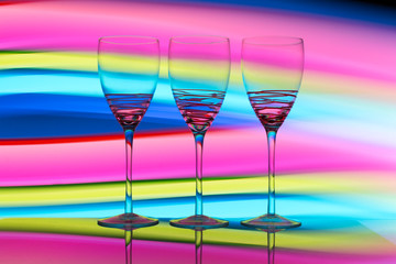 Three empty wine glasses in a row with colorful light painting behind