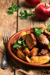 Hot pork stew with apple slice on the plate, vintage wooden kitchen table background, selective focus
