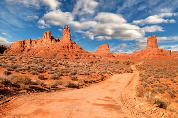 Road leads through Valley of the Gods in central Utah with red rocks and clouds