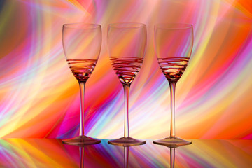 Three empty wine glasses in a row with colorful light painting behind