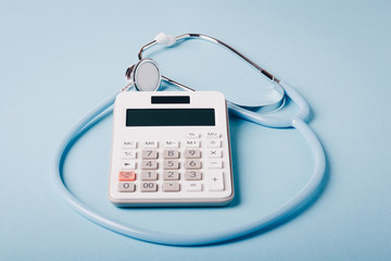 White calculator and blue stethoscope on a blue background as a symbol of paid (expensive) medicine