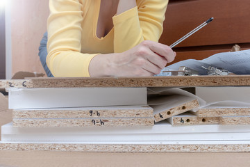 Woman sitting on the floor at home and assembling furniture using hand tools