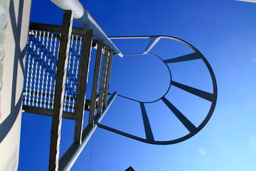 Blick von unten auf eine Leiter mit Sicherungsbügel. Der Blick Symbolisiert den Aufstieg mit...