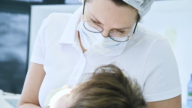 Woman Dentist doctor in glasses mask and white cap examines the oral cavity of the patient. Dentist's work