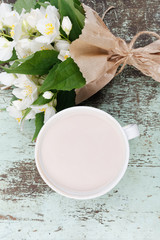 A cup of coffee with milk and flowers. Bouquet of jasmine flowers on wooden background.