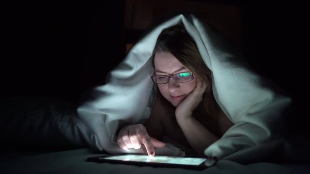 Young woman using tablet on the bed before she sleeping at night. Mobile addict or insomnia concept.